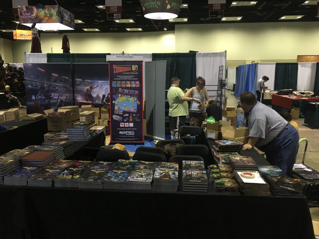Jonathan Thompson, Emily Knight, Adam Thompson, and me hiding on the floor with bookshelves working on Modiphius booth for Gen Con 2016. Daughter Rachel taking the picture. 