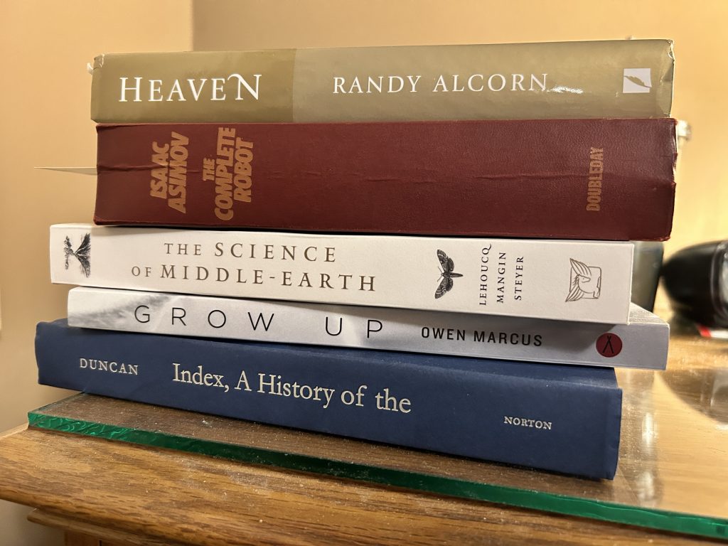 Current reading pile including Heaven by Randy Alcorn, The Complete Robot by Isaac Asimov, The Science of Middle Earth by Lehoucq, Grow Up by Owen Marcuc, and Index, A History of the by Duncan. 