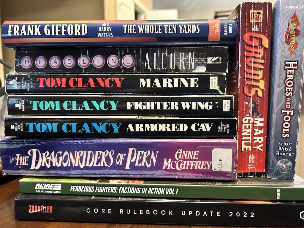 My to be read pile for the 2023 holidays including The Whole Ten Yards by Frank Gifford, Deadline by Alcorn, Marine by Clancy, Fighter Wing by Clancy, Amored CAV by Clancy, Dragonriders of Per by McCaffrey, Grunts by Gentle, Heroes and Fools by Weis and Kickman, G.I.Joe RPG Ferocious Fighters, and Traveller Core Rulebook Update 2022